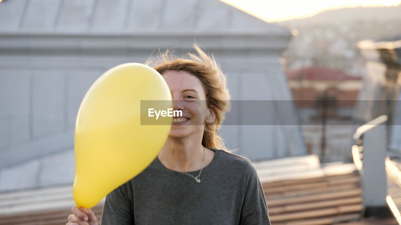 Woman holding balloon while standing on roof during sunset