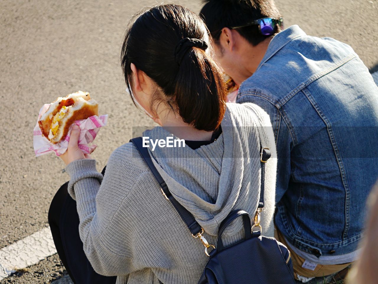 Rear view of man and woman eating burger while sitting outdoors