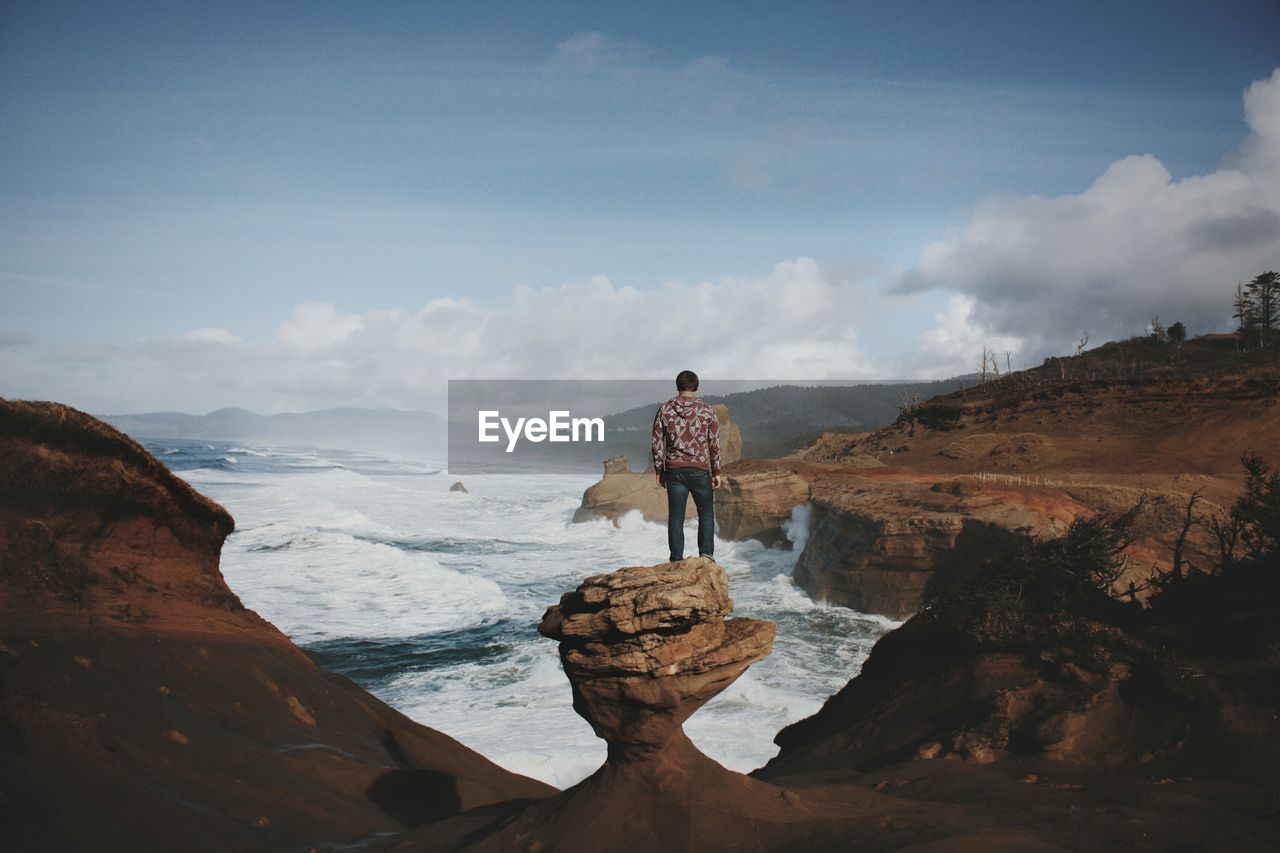 Hiker standing on rock while looking at sea amidst rock formation against sky