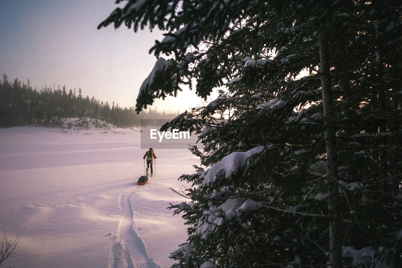 Skier pulling pulk sled walking across a frozen lake at sunrise