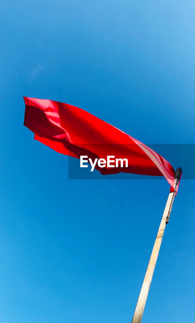 Low angle view of red flag against clear blue sky