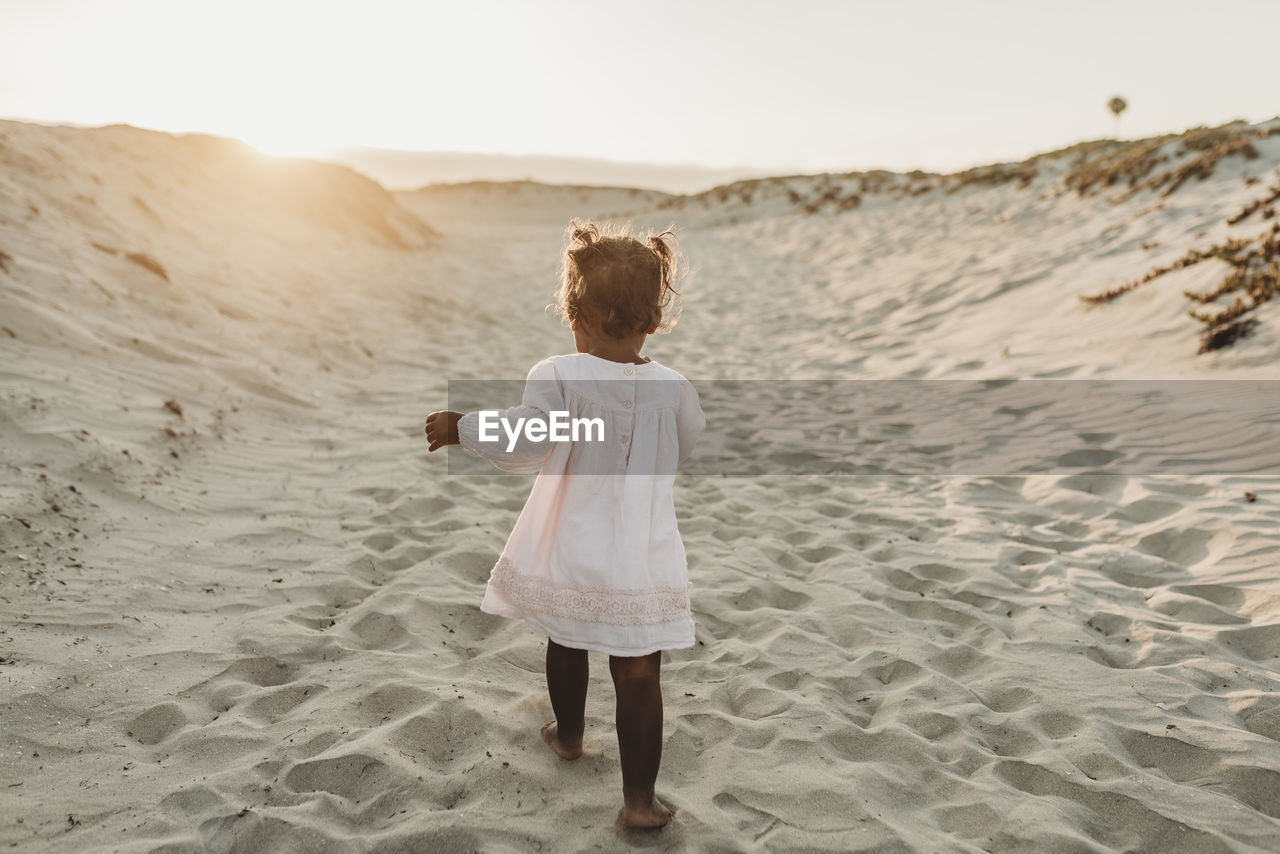 Behind view of young girl walking away at beach during sunset