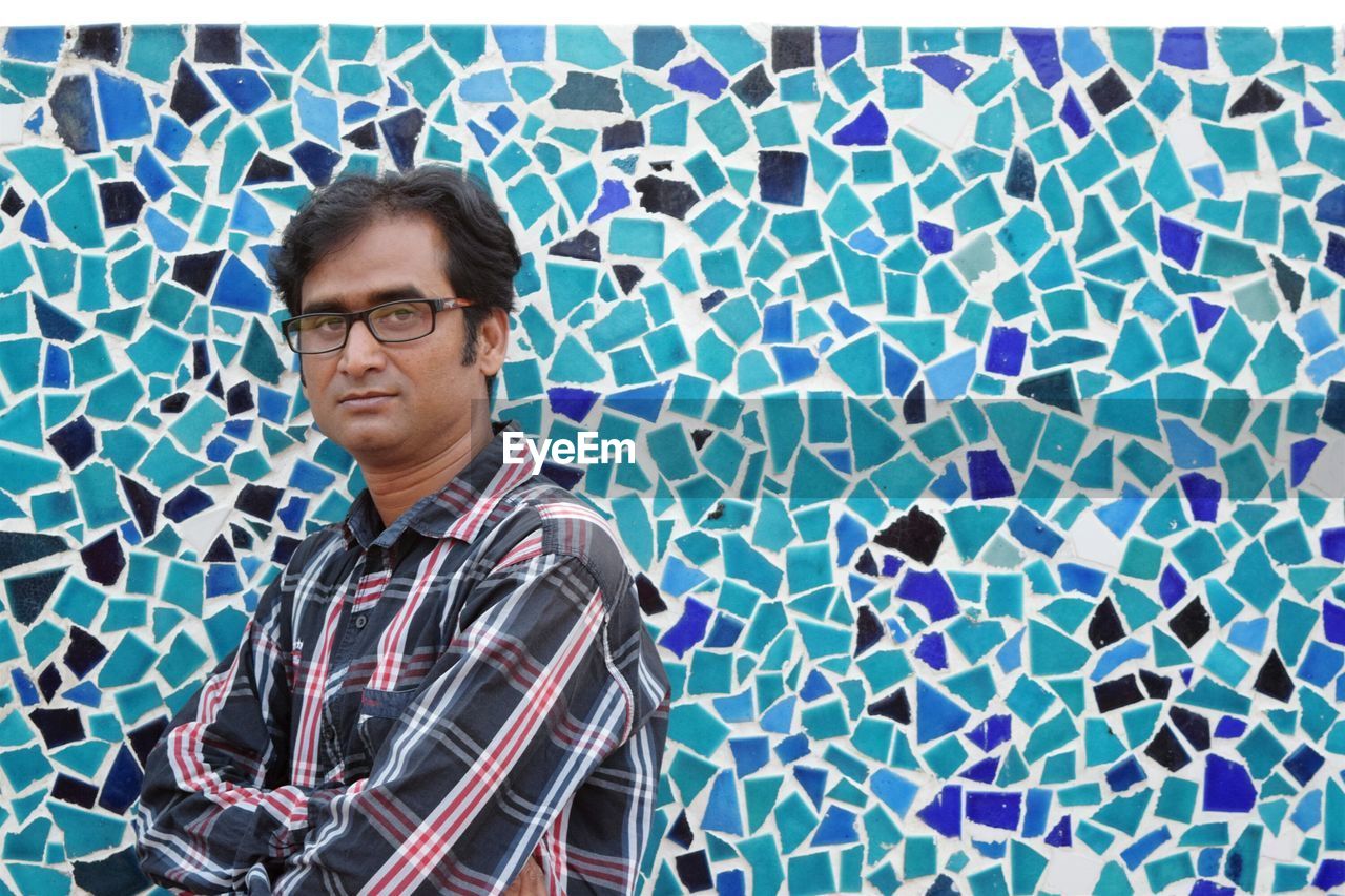 Portrait of man with arms crossed against mosaic wall