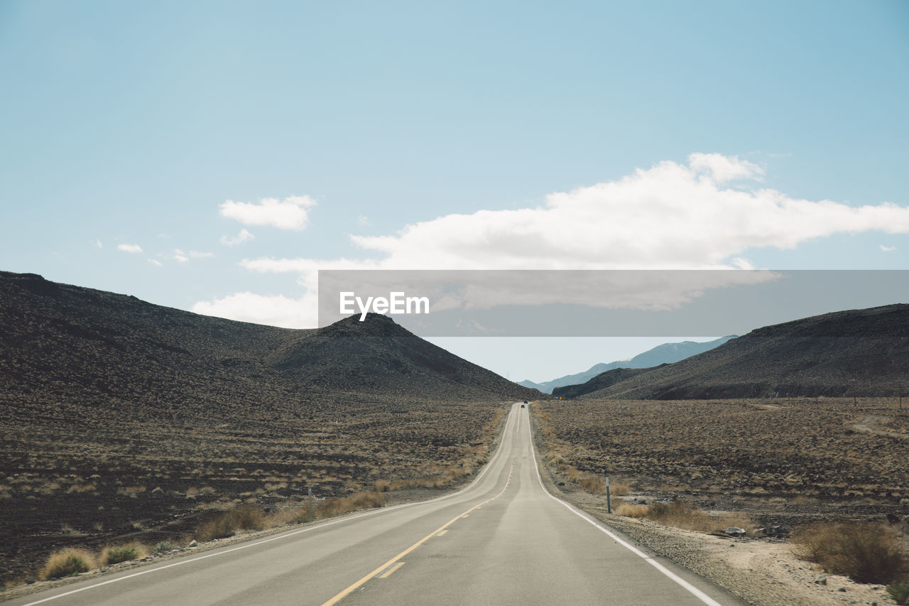 Empty road leading towards death valley mountains against sky