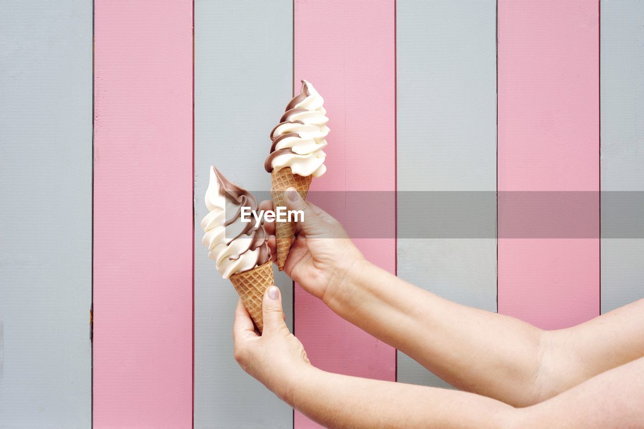 Cropped hands holding ice cream cones against wall