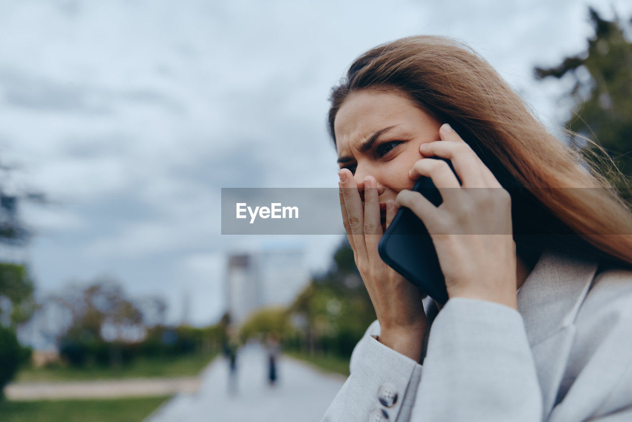 young woman using mobile phone against sky