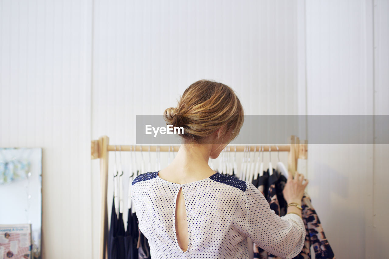 Rear view of woman arranging clothes in rack