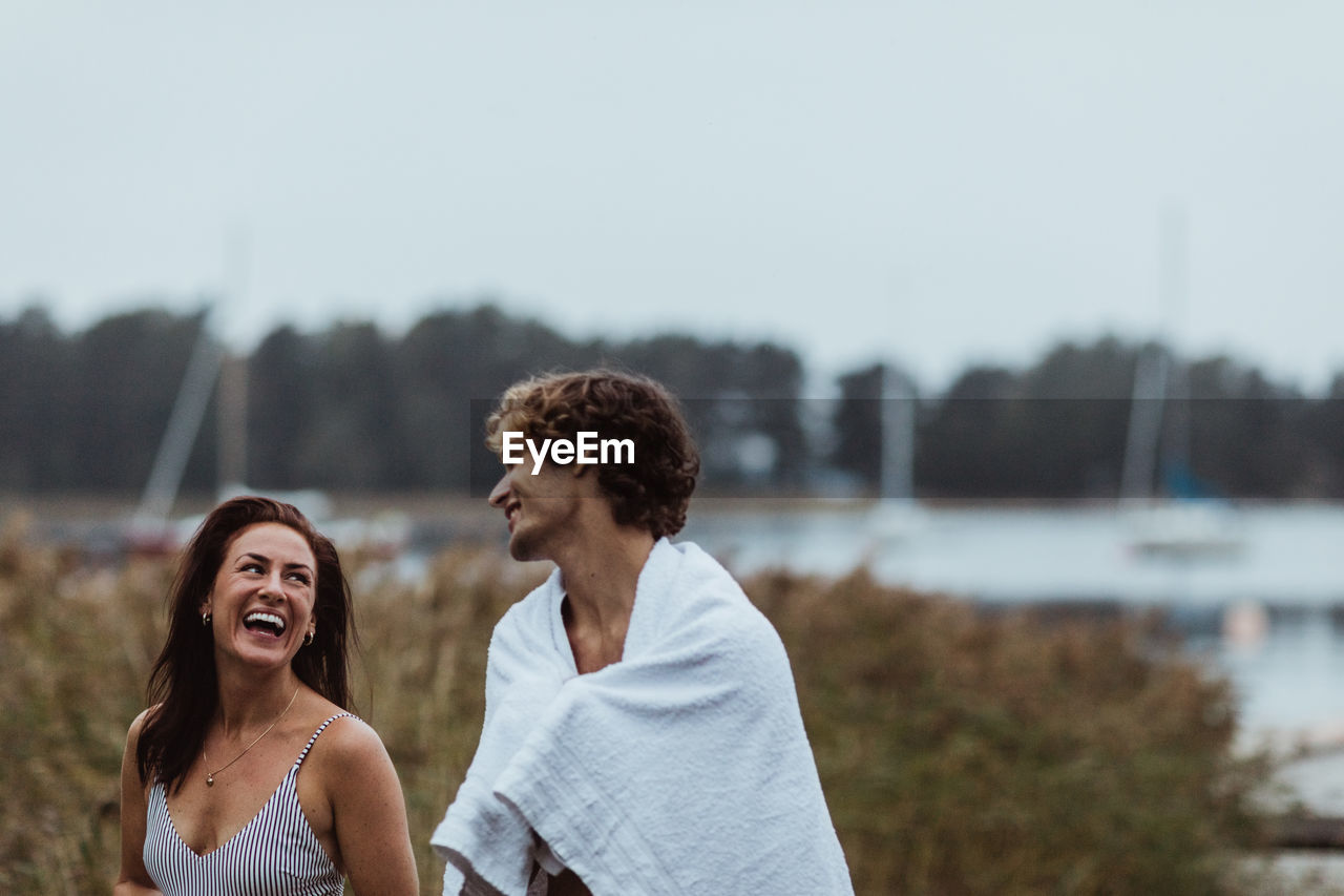 Smiling young man standing with woman by sea against sky