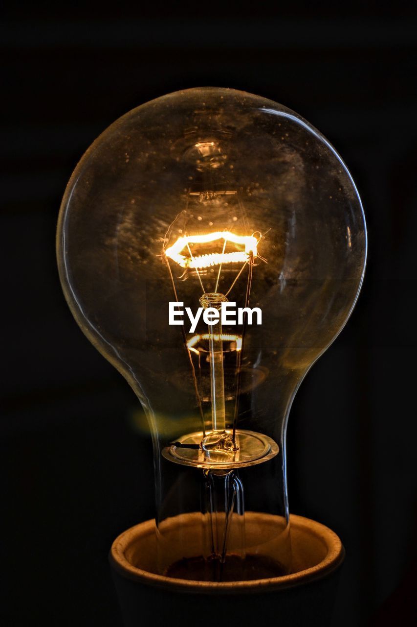 Close-up of illuminated light bulb over black background