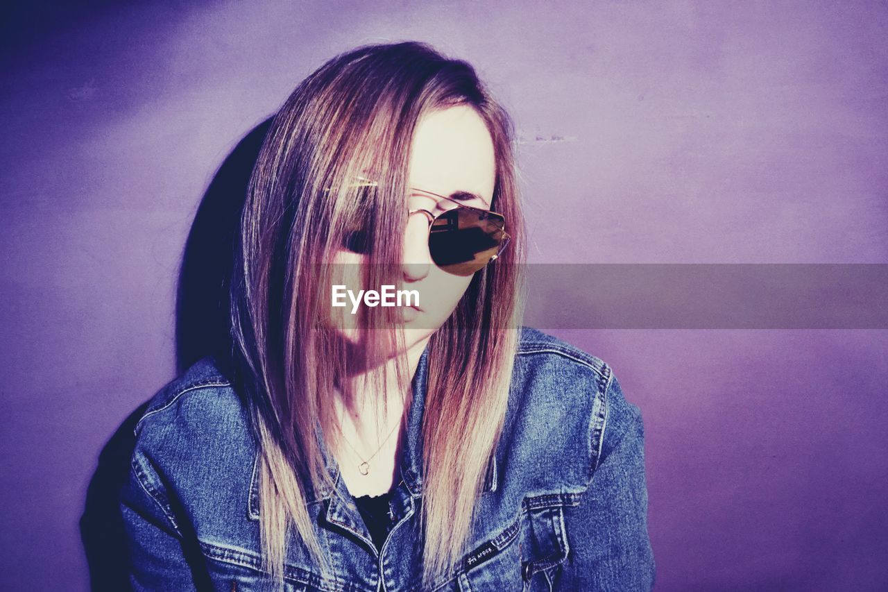 Portrait of young woman in sunglasses against purple background
