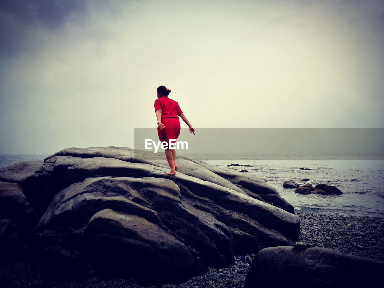 Rear view full length of woman standing on rock at beach against sky