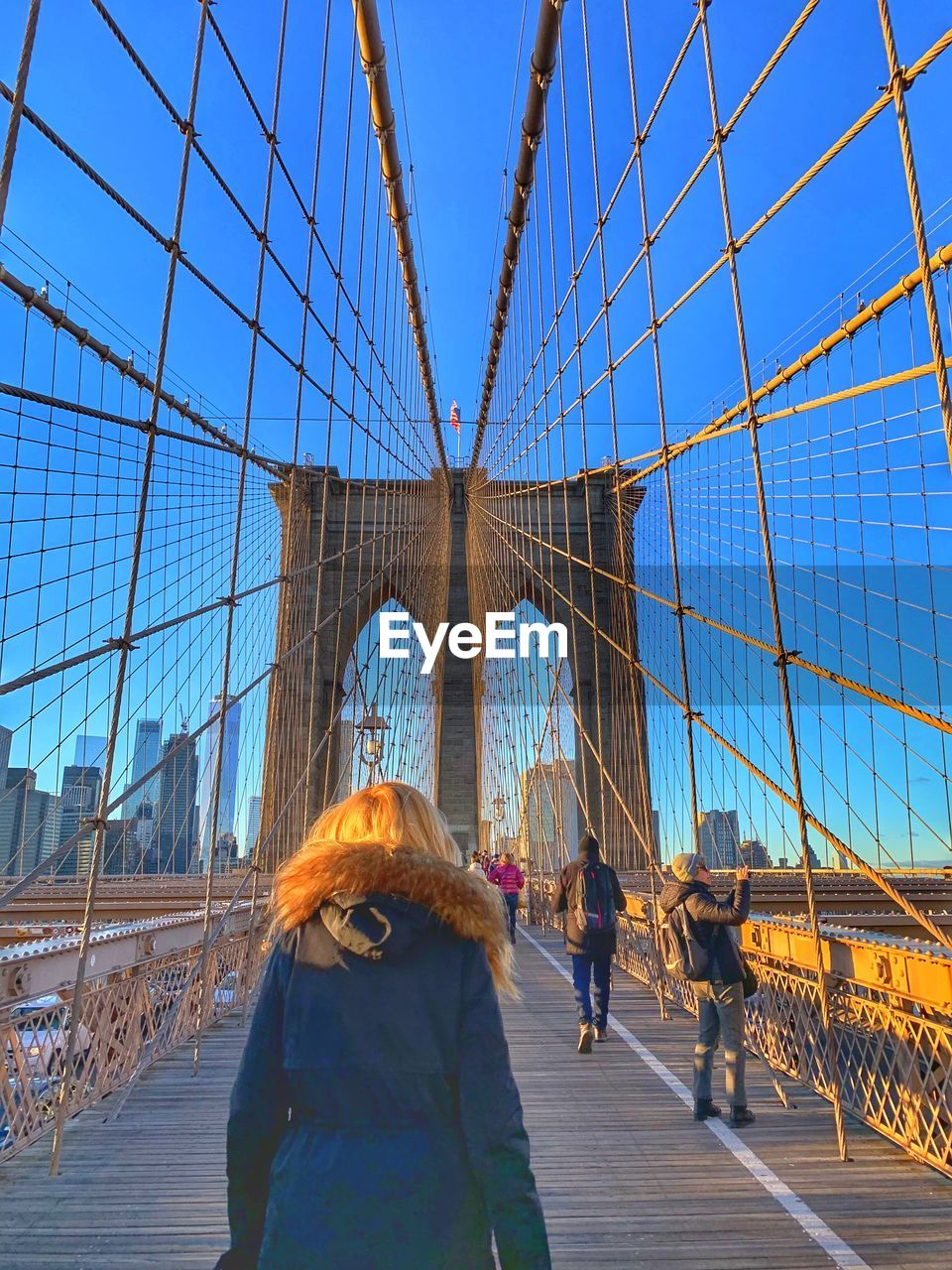 PEOPLE WALKING ON SUSPENSION BRIDGE AGAINST SKY