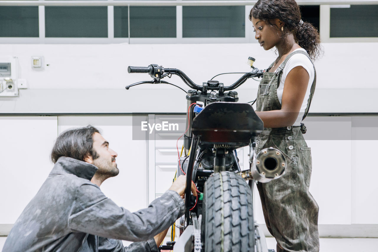 Diverse male and female mechanics in workwear fixing motorcycle together in bright garage