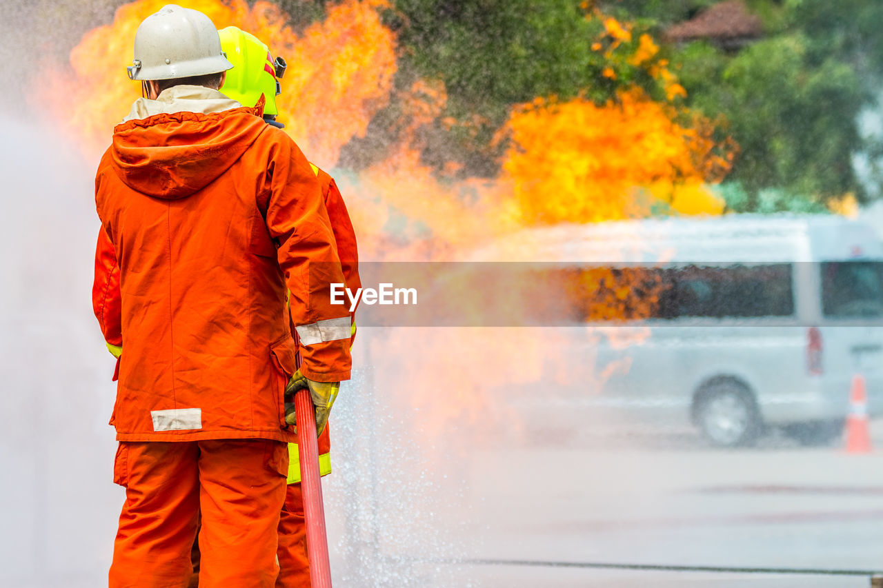 Rear view of firefighters spraying water on fire