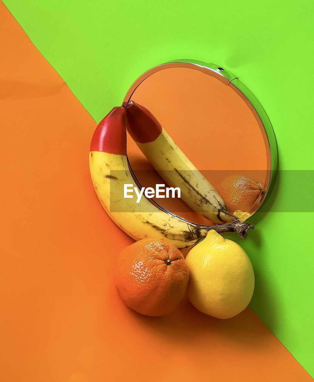High angle view of fruits on mirror on orange and green background.