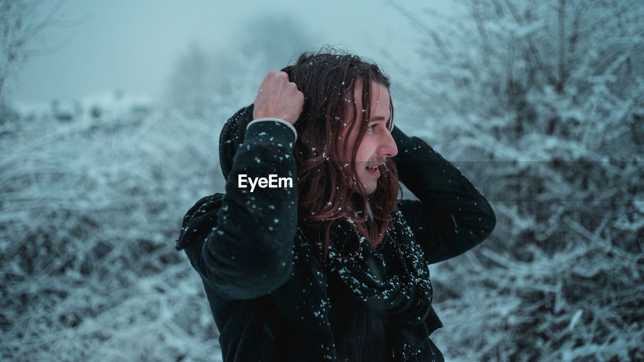 Smiling young man with snow on body standing in forest during winter