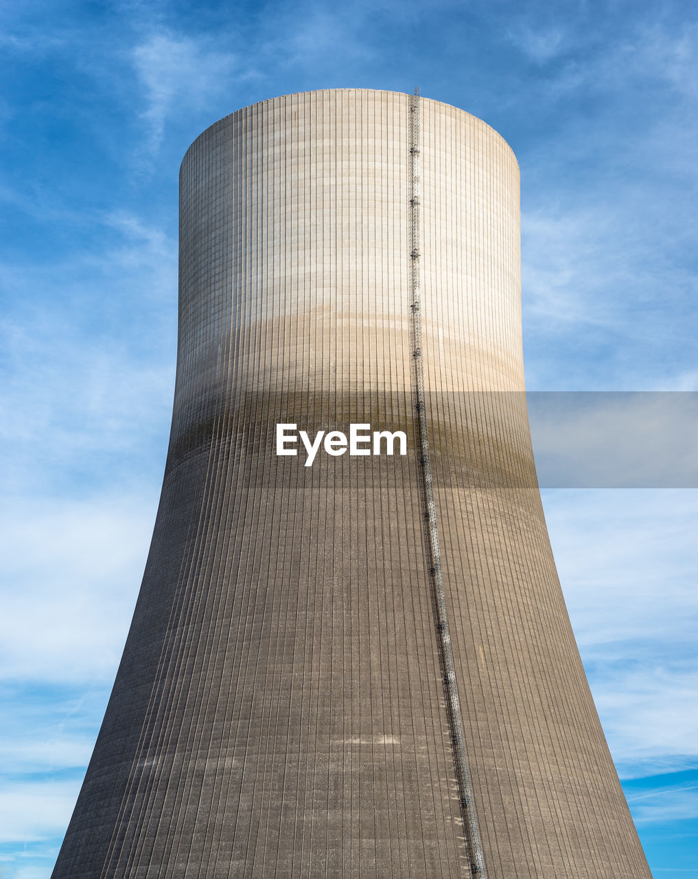 A huge chimney of a nuclear power plant close up on a background of blue sky with clouds.