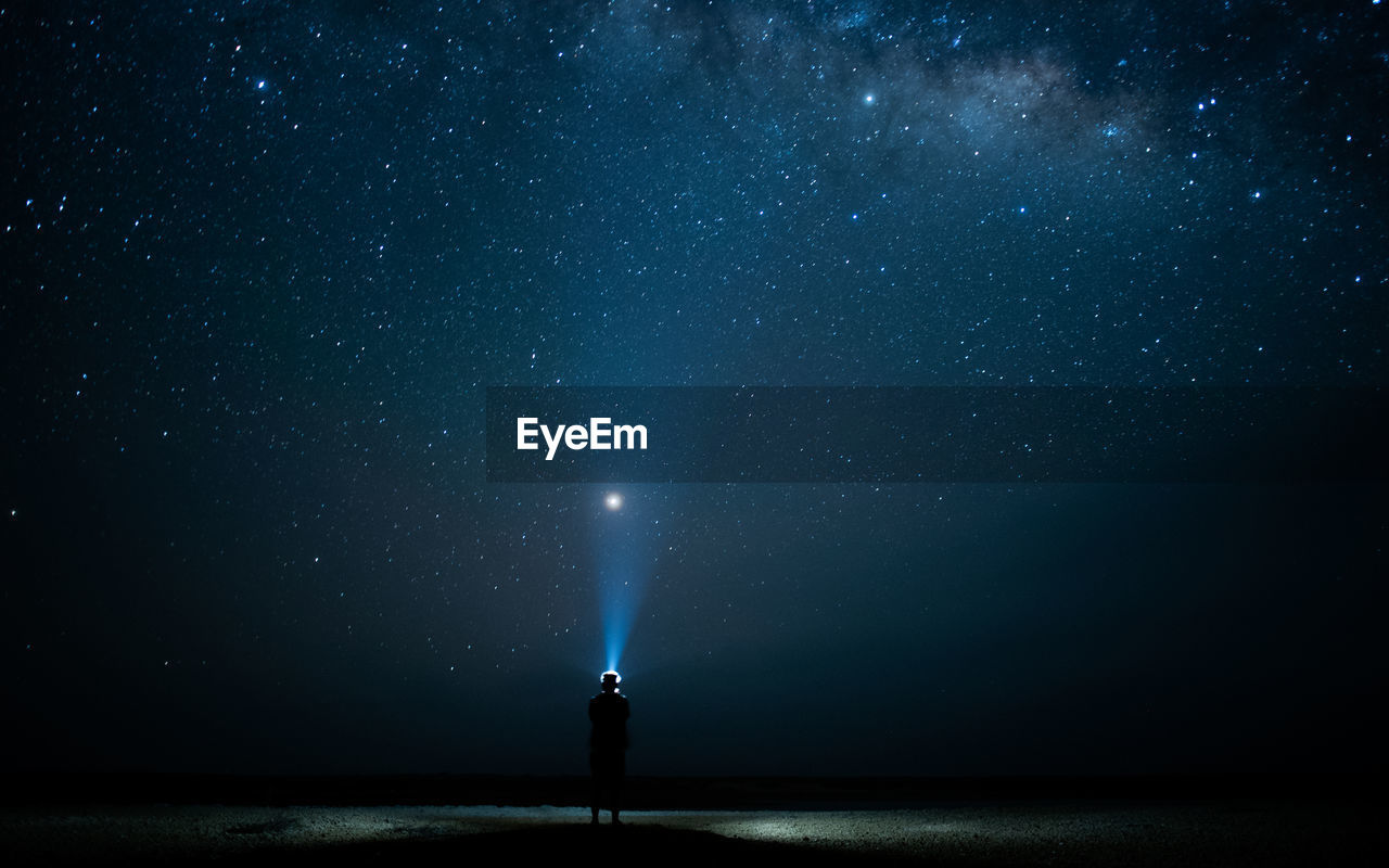 Rear view of man flashing light in sky at night