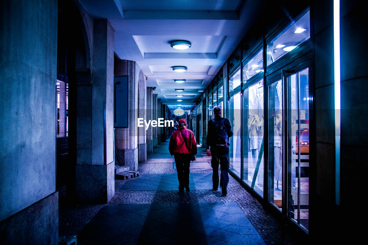 Rear view full length of man and woman walking by store in corridor