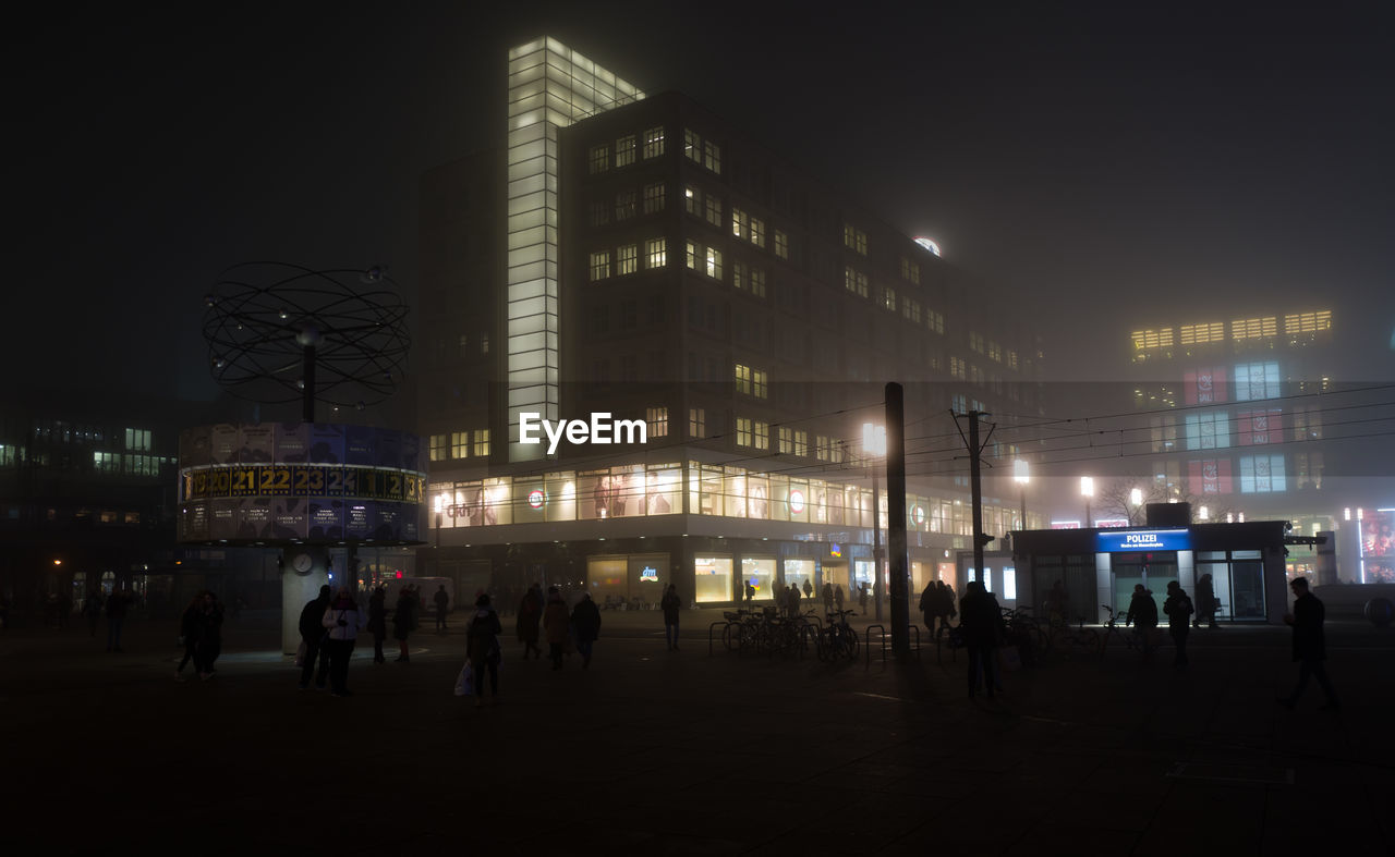 PEOPLE IN ILLUMINATED CITY AGAINST SKY