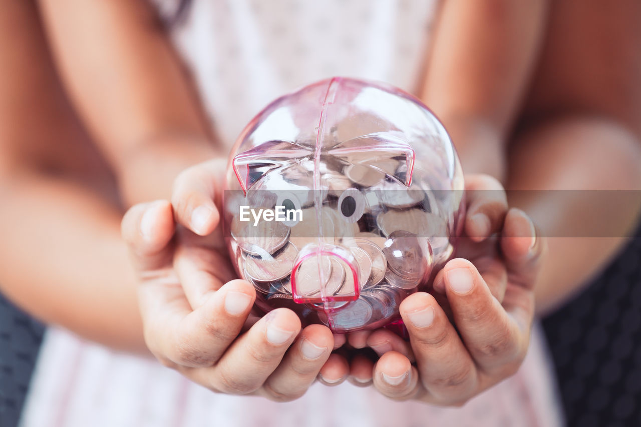 Midsection of mother and daughter holding piggy bank