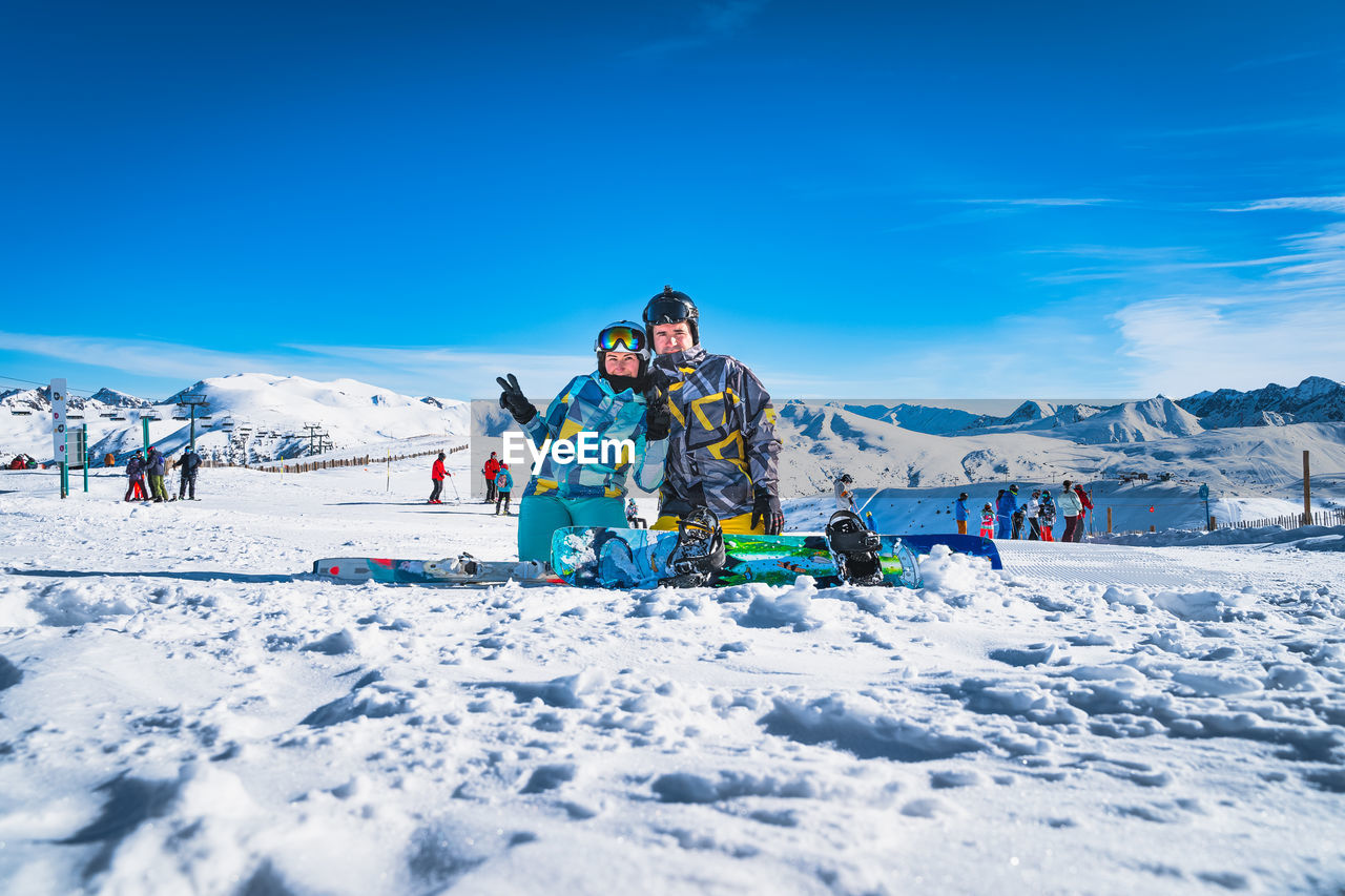 Couple, skier and snowboarder sitting on the snow and looking at camera, pyrenees mountains, andorra