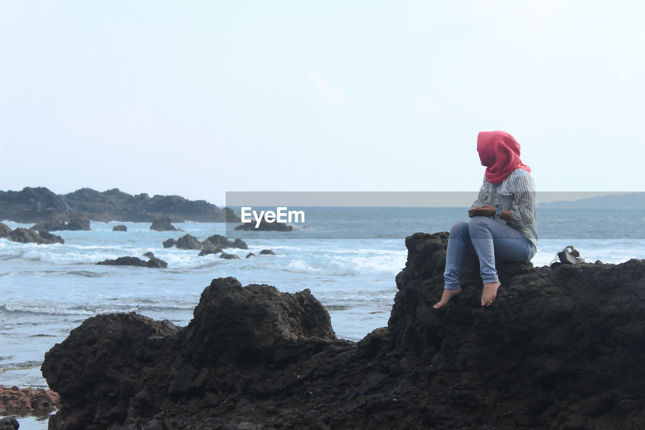 People sitting on rock by sea against sky