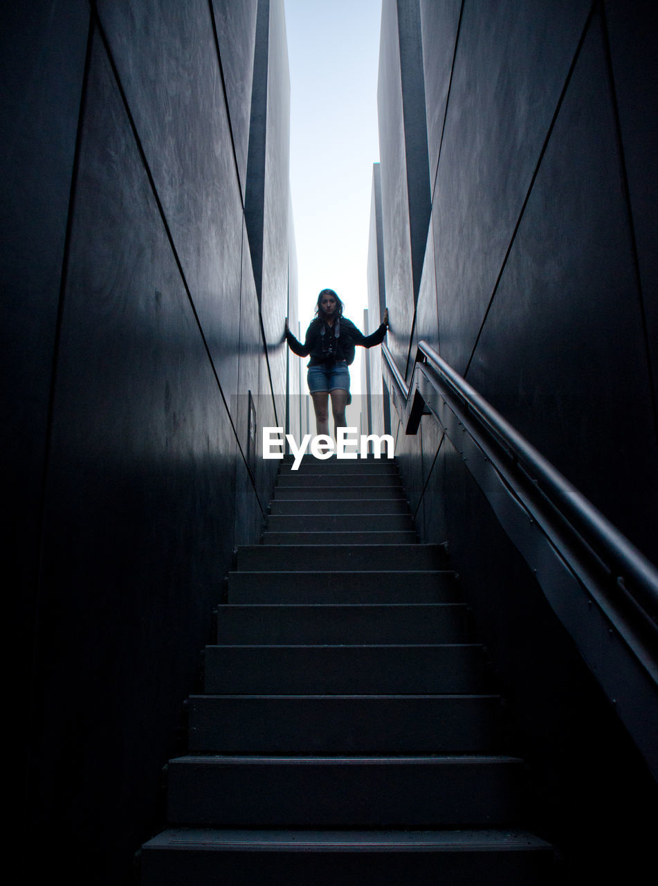 Low angle view of woman standing on steps amidst walls