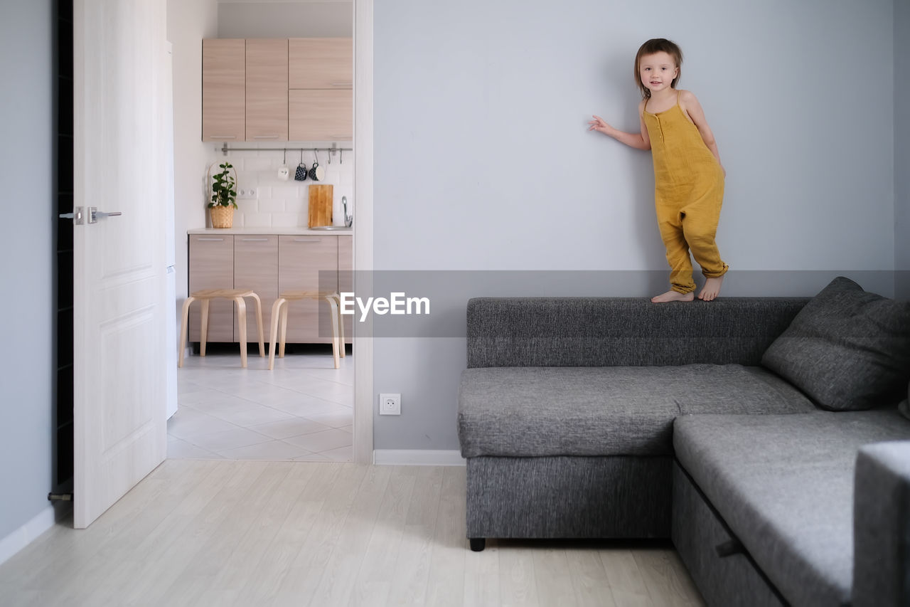 Child jumps and plays on sofa in minimalist living room, gray sofa.