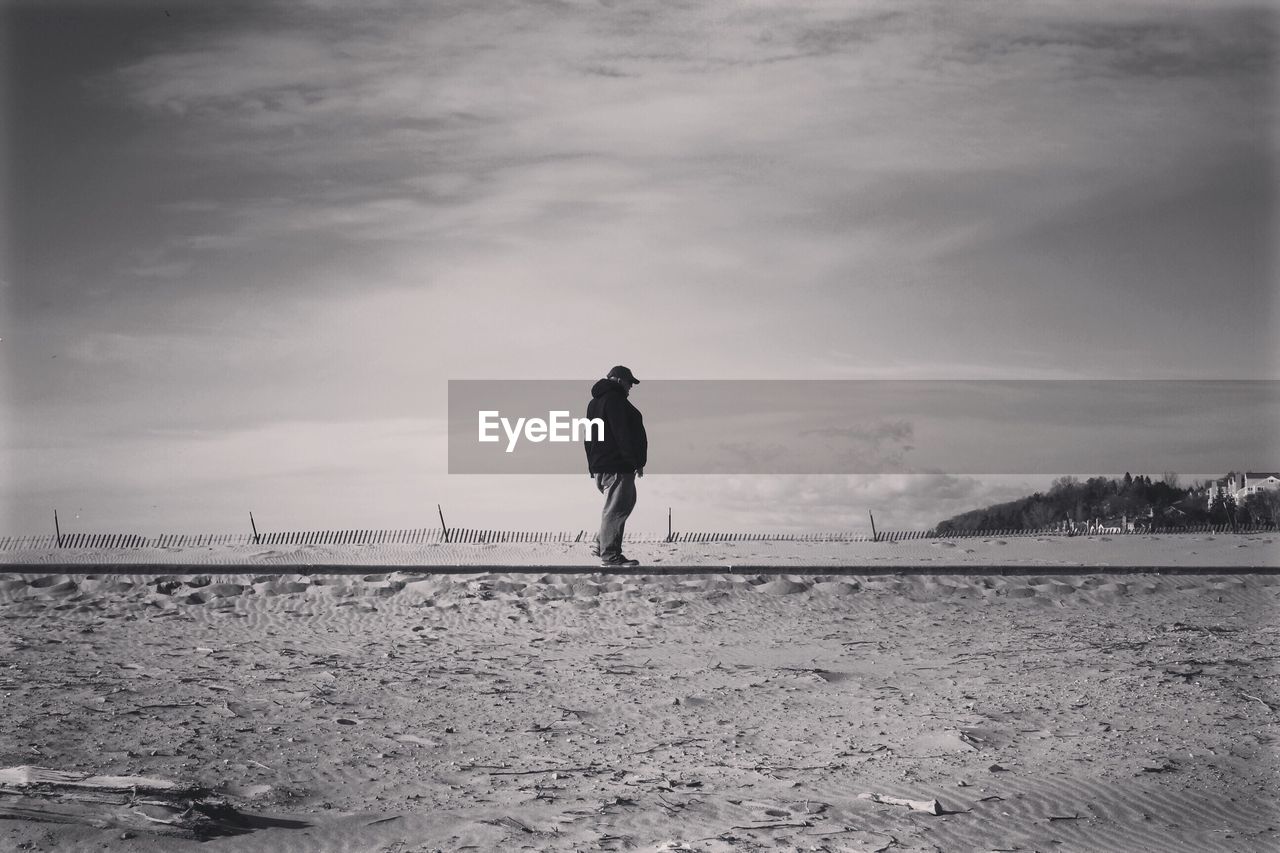 Man standing at beach against cloudy sky