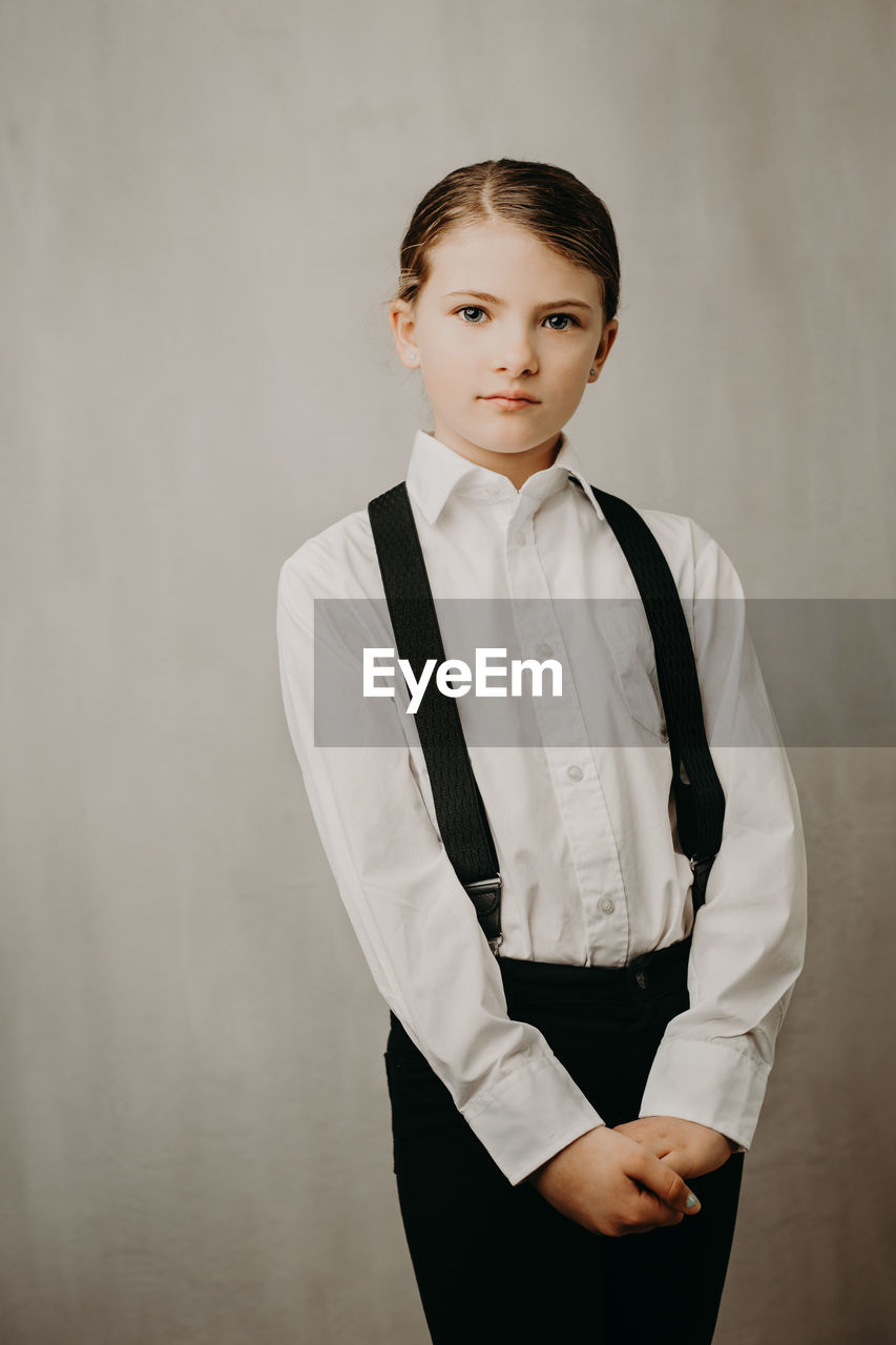 Portrait of girl wearing suspenders and shirt against white background