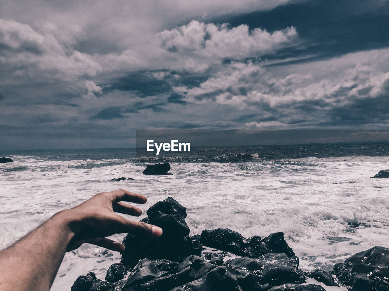 Optical illusion of cropped hand reaching for rock against sea