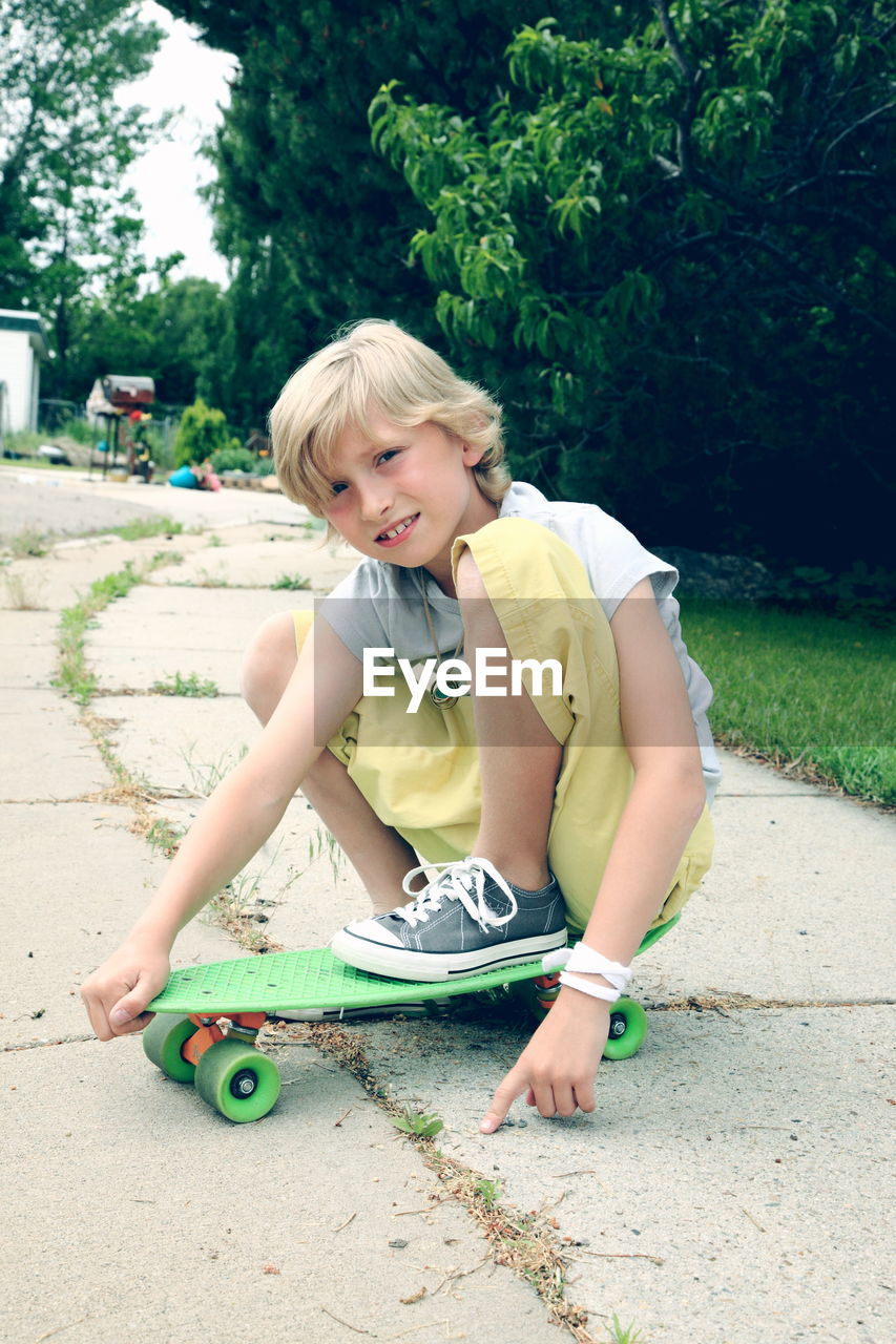 Portrait of boy crouching on skateboard at park