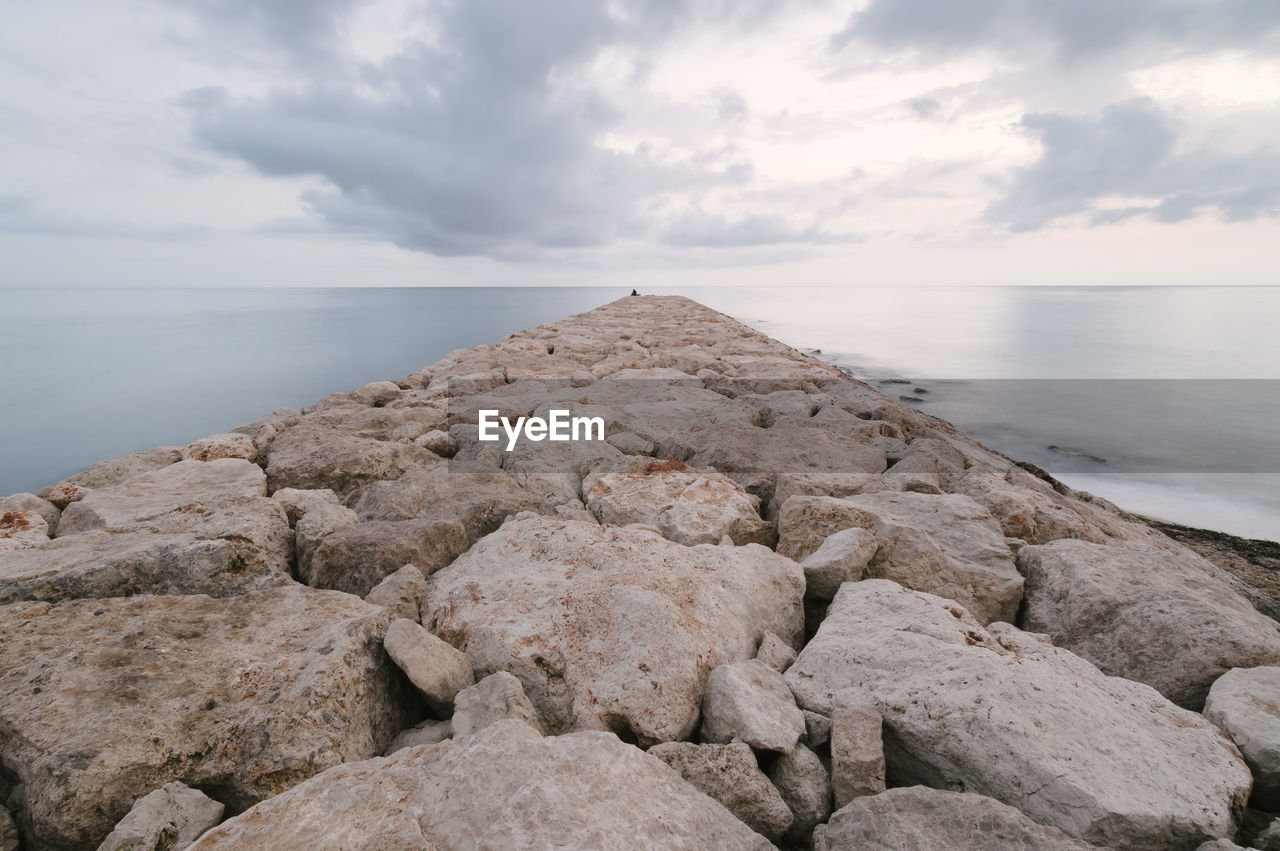 Rocky pier in sea against sky