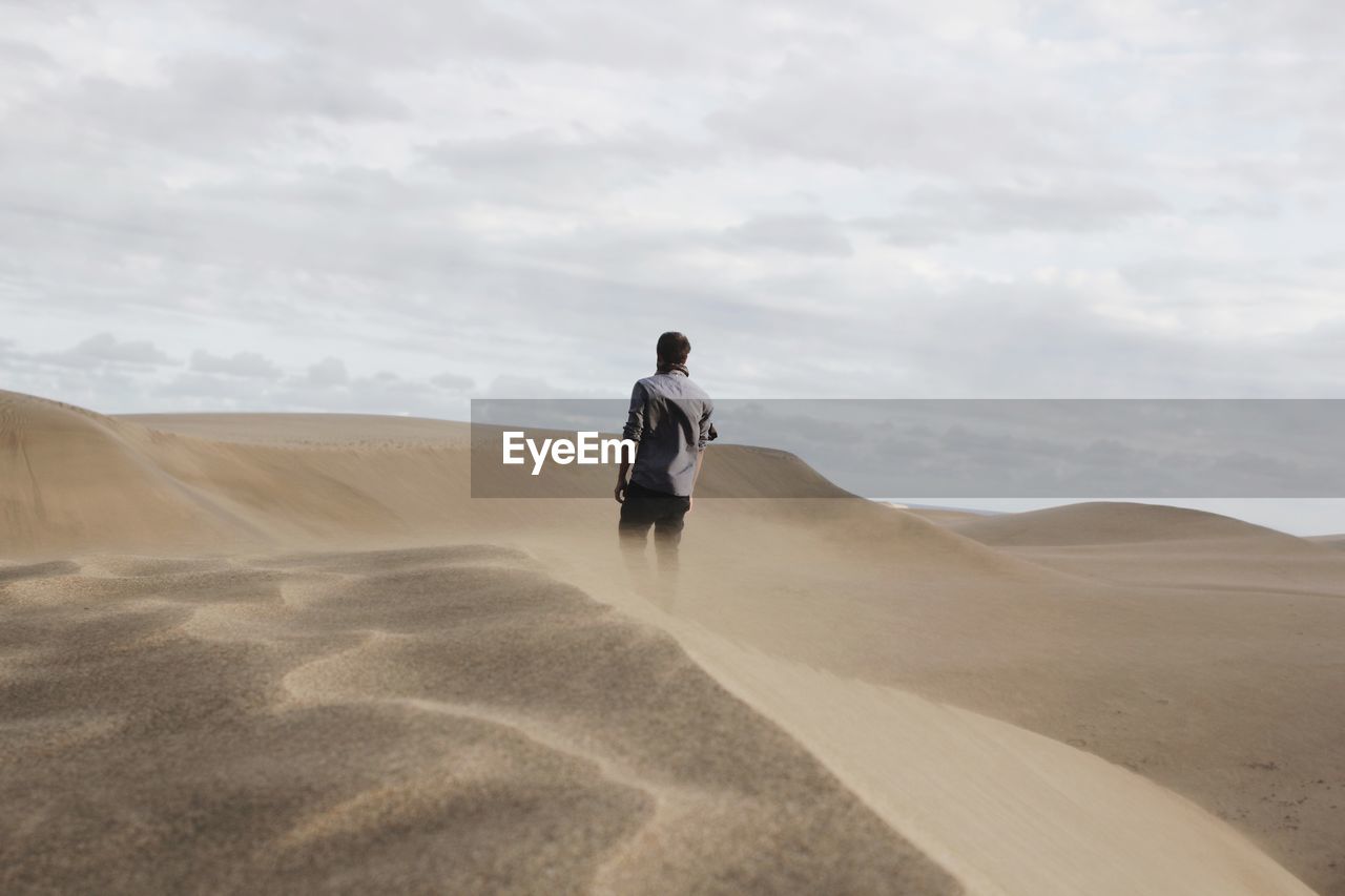 Rear view of man walking on sand dune at desert