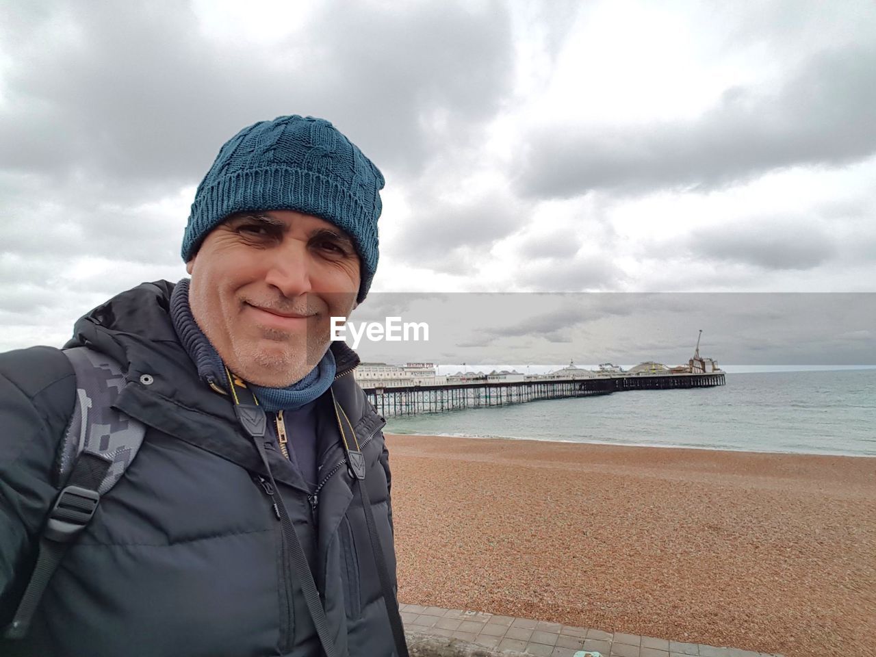 cloud, smiling, portrait, water, one person, sea, sky, adult, looking at camera, happiness, clothing, nature, emotion, land, beach, men, overcast, holiday, vacation, day, cheerful, trip, mature adult, human face, hat, standing, front view, person, leisure activity, outdoors, travel, teeth, smile, travel destinations, senior adult, waist up, occupation, winter, sports, transportation, lifestyles, jacket, nautical vessel