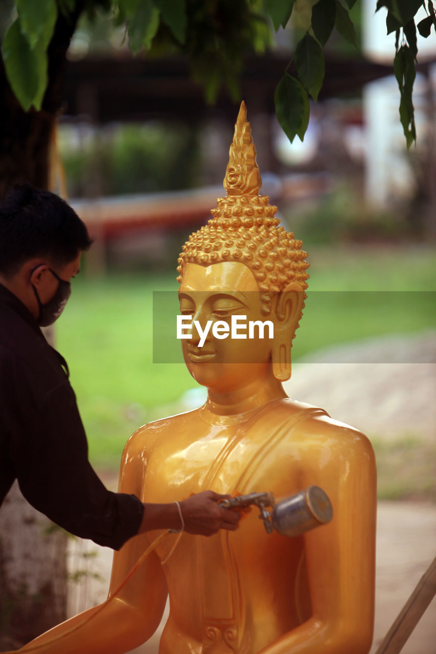 Close-up of man painting lord buddha statue