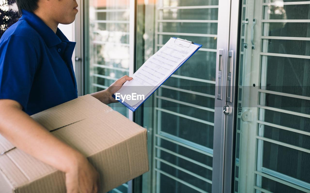 Midsection of delivery man holding paper and package while standing at entrance