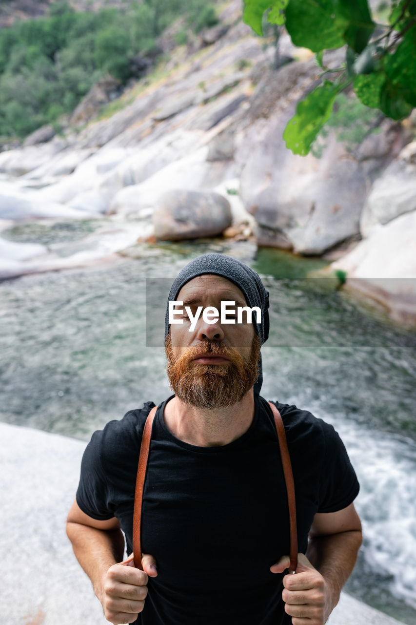 High angle of carefree male traveler standing on rock near rapid river and enjoying freedom during summer vacation