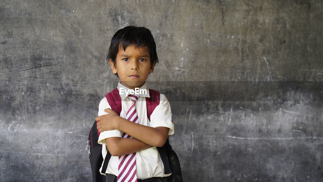 Indian school boy standing against blank chalkboard, intelligent and smart student