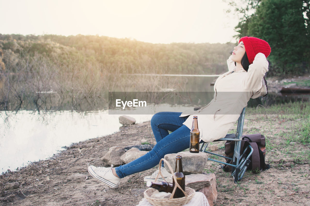 Side view of woman sitting on folding chair by lake