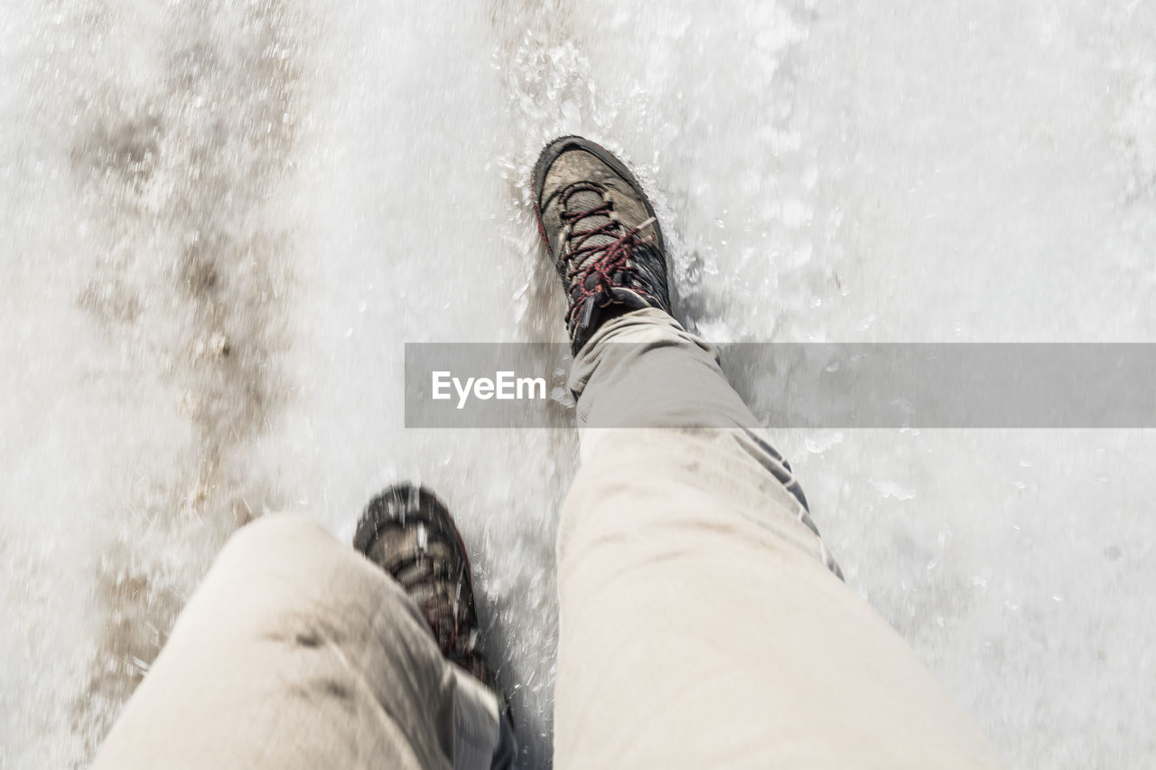 Low section of mid adult man walking on snow covered field