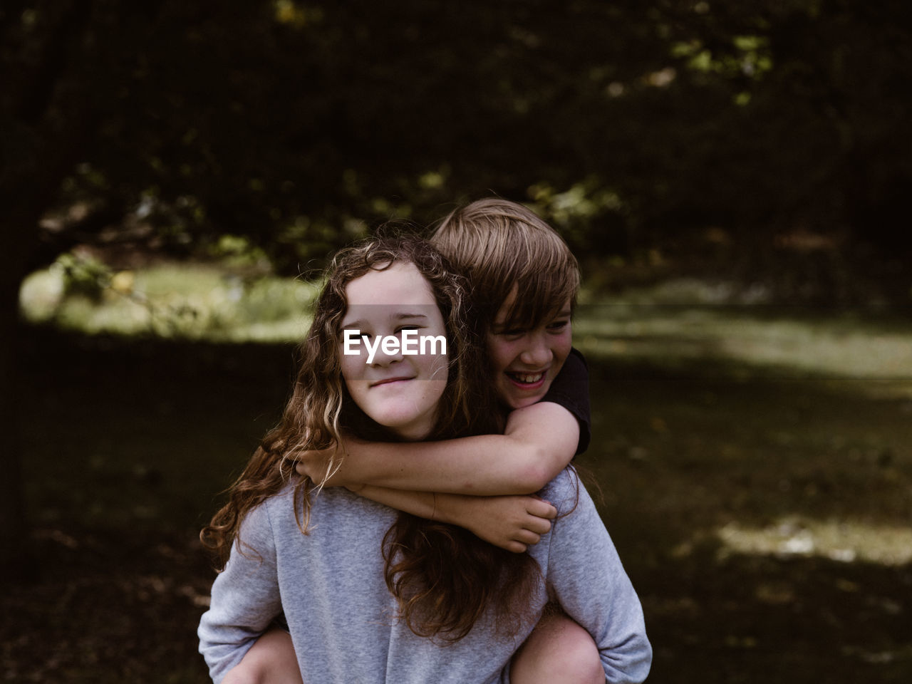 Portrait of smiling sister piggybacking brother in forest