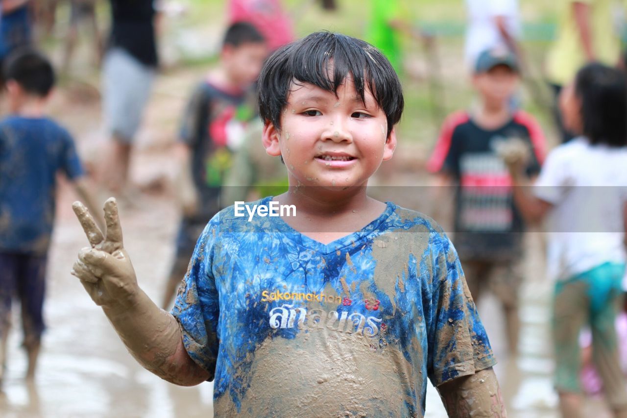 Cute boy covered in mud while gesturing peace sign outdoors
