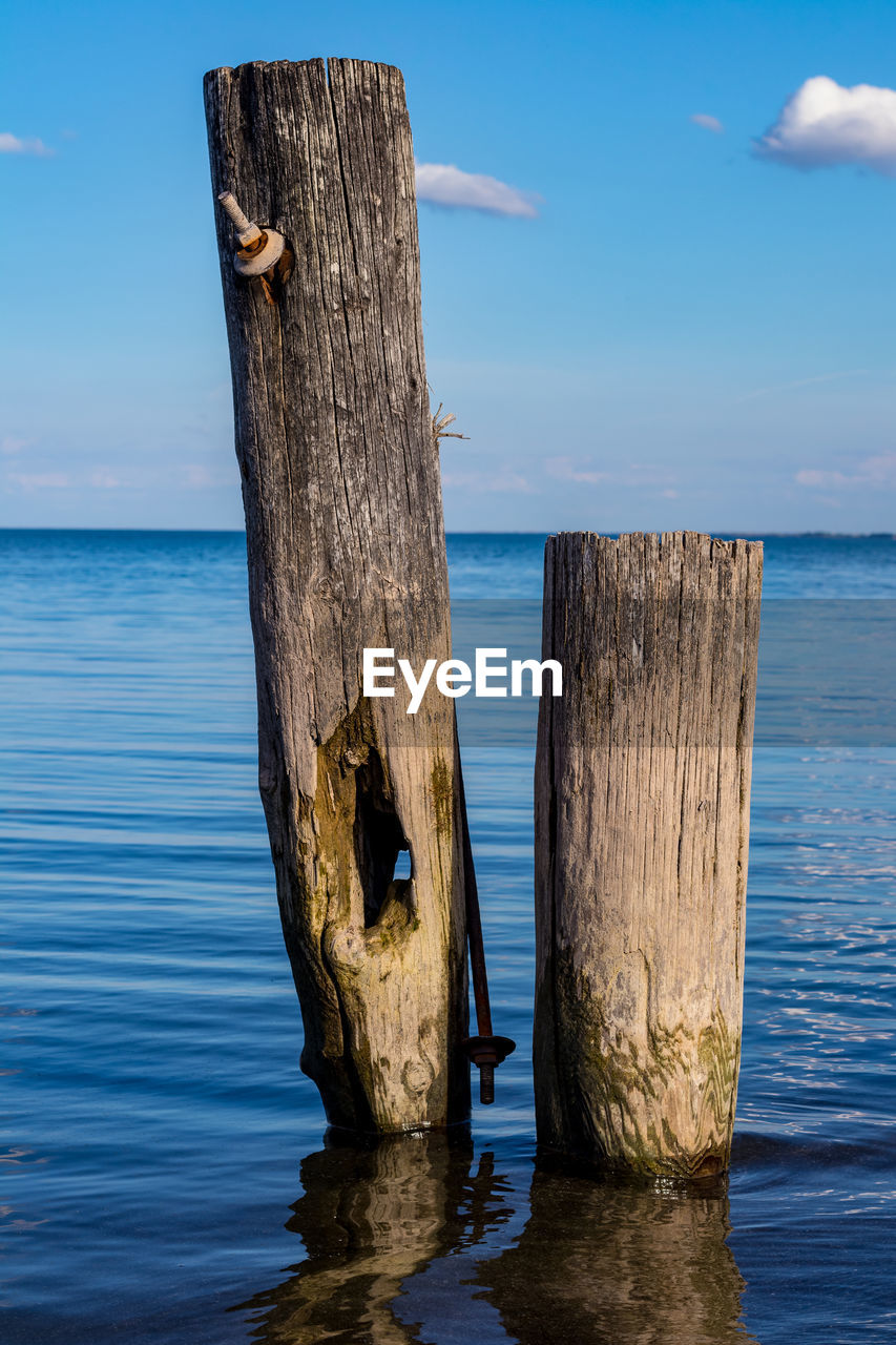 Wooden posts on sea against sky