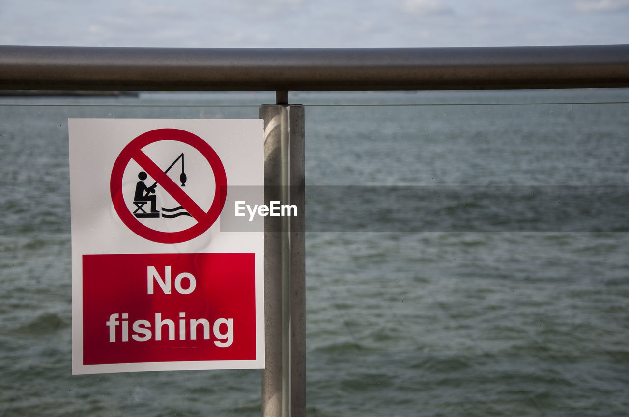 Close-up of sign board on railing against sea