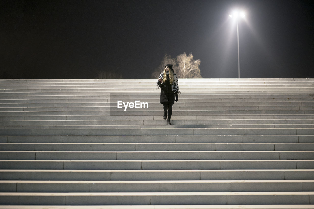 FULL LENGTH REAR VIEW OF WOMAN WALKING ON ILLUMINATED STAIRCASE