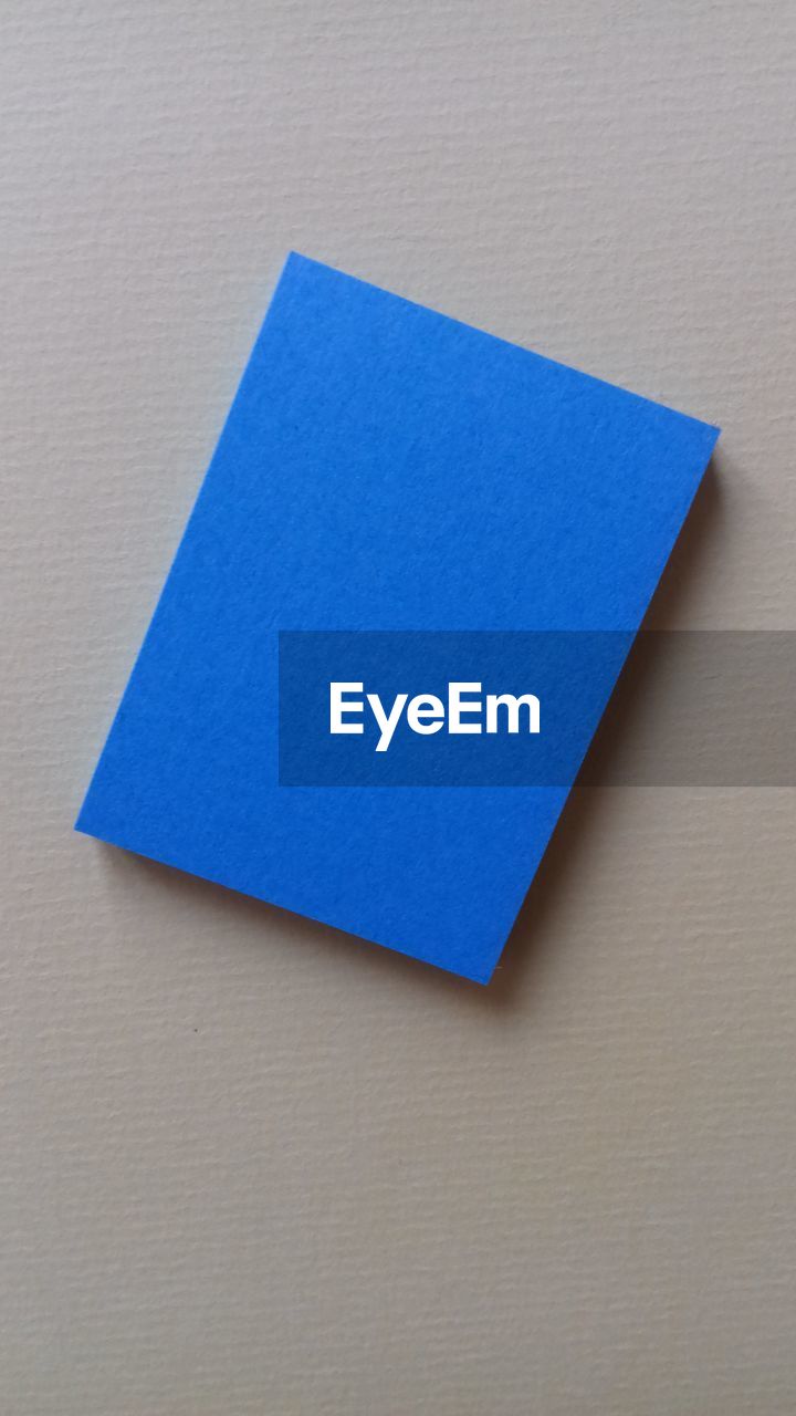 HIGH ANGLE VIEW OF BLUE PAPER AGAINST WHITE WALL