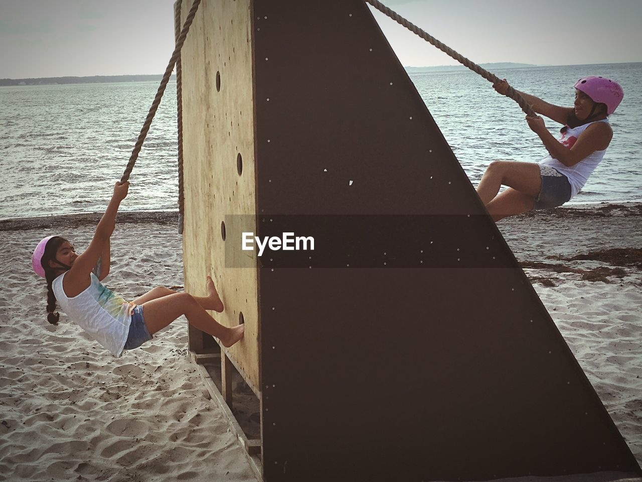 Side view of female friends climbing with rope on wall at sandy beach