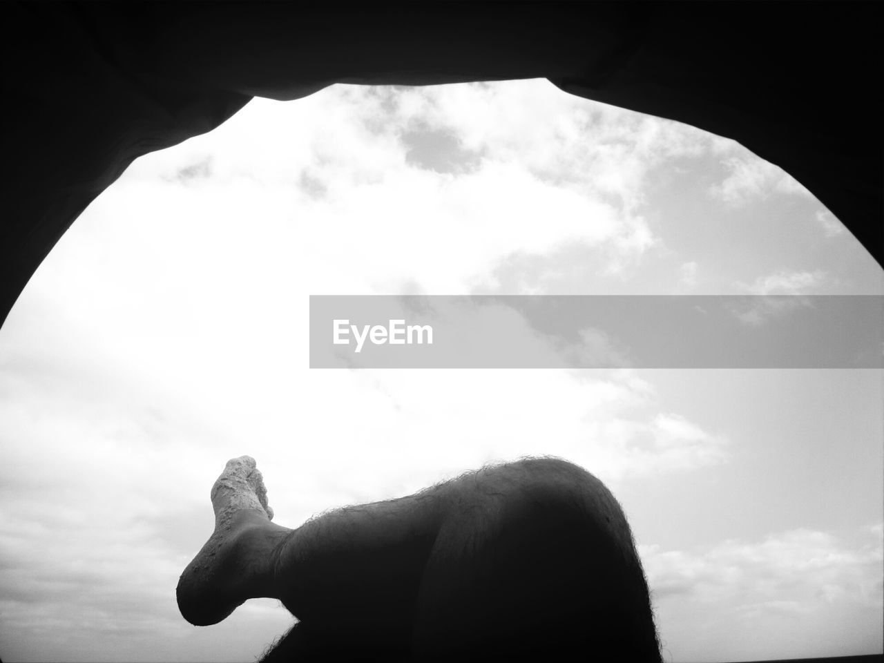 Low section of man relaxing in cave against sky